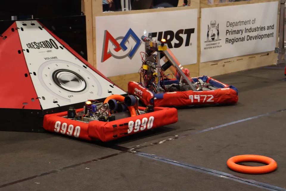 Two red-bumpered robots, numbered 9990 and 1972, on the competition field beside an orange ring.