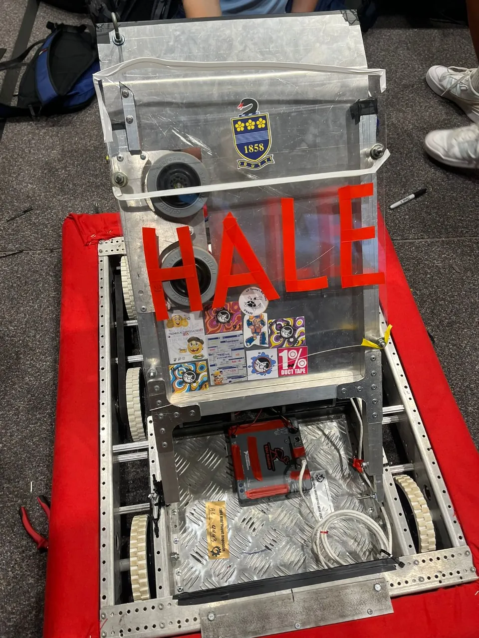 A tall robot with a clear cover and a red HALE sign, on a red-bordered pad.